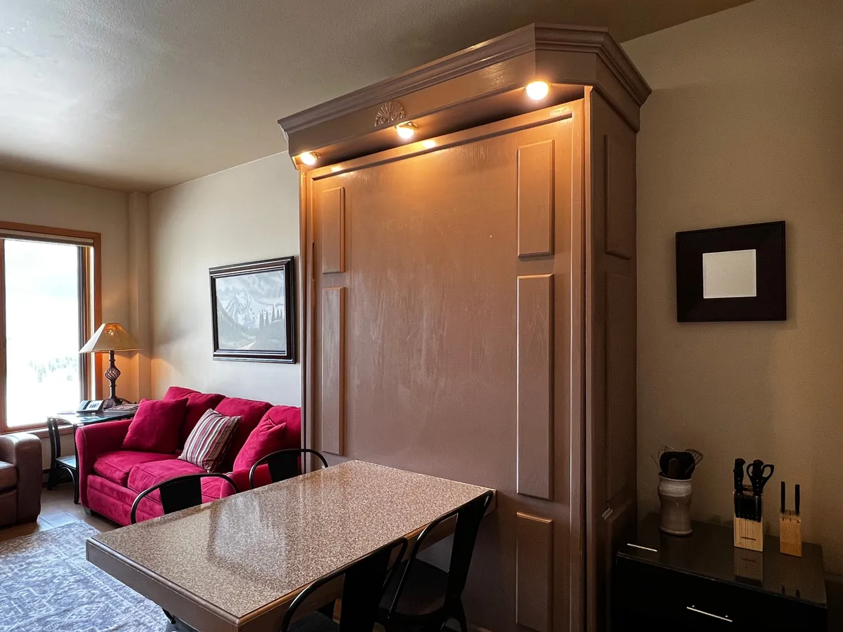 A welcoming living and dining area with a plush red sofa, a granite dining table, large wall cabinet, and tasteful artwork. The scene invites socializing, relaxation, and spontaneous gatherings, offering a sense of home in the heart of the action.