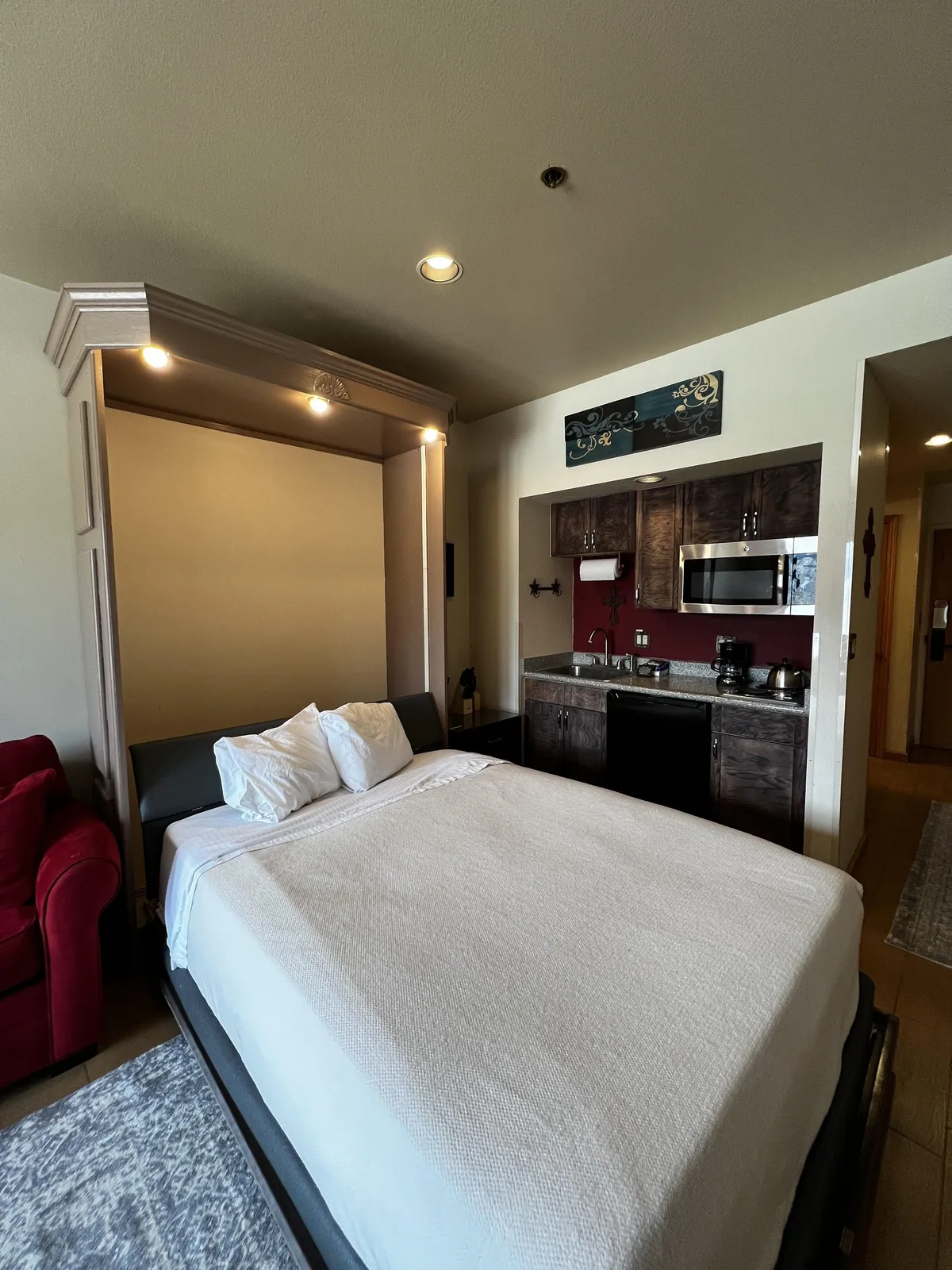 This cozy interior scene features a comfortable bed, a vibrant red couch, and a well-equipped kitchenette. The space feels lived-in and inviting, suggesting a blend of relaxation, cooking, and casual entertaining. The elements in view reinforce the idea of a home away from home, with everything needed for daily routines.