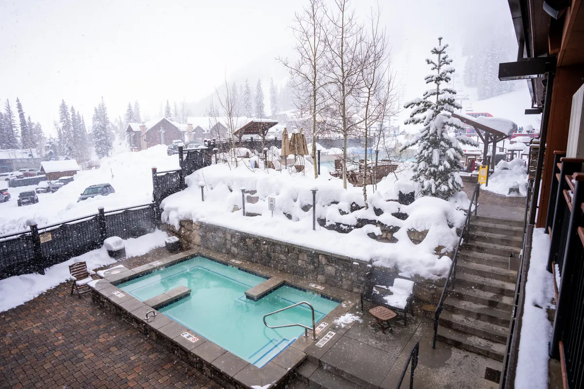 An inviting rooftop hot tub set against a stunning snow-covered landscape, surrounded by trees and an outdoor seating area. The steam from the hot tub mingles with the crisp winter air, creating a tranquil atmosphere perfect for stargazing or unwinding after a day on the slopes.