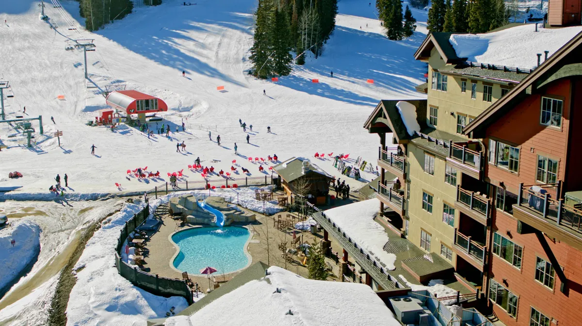 A broad exterior view featuring the ski slopes, a swimming pool, a ski lift, and the hotel building in the background. The scene shows skiers and swimmers, encapsulating a full spectrum of après-ski activities.
