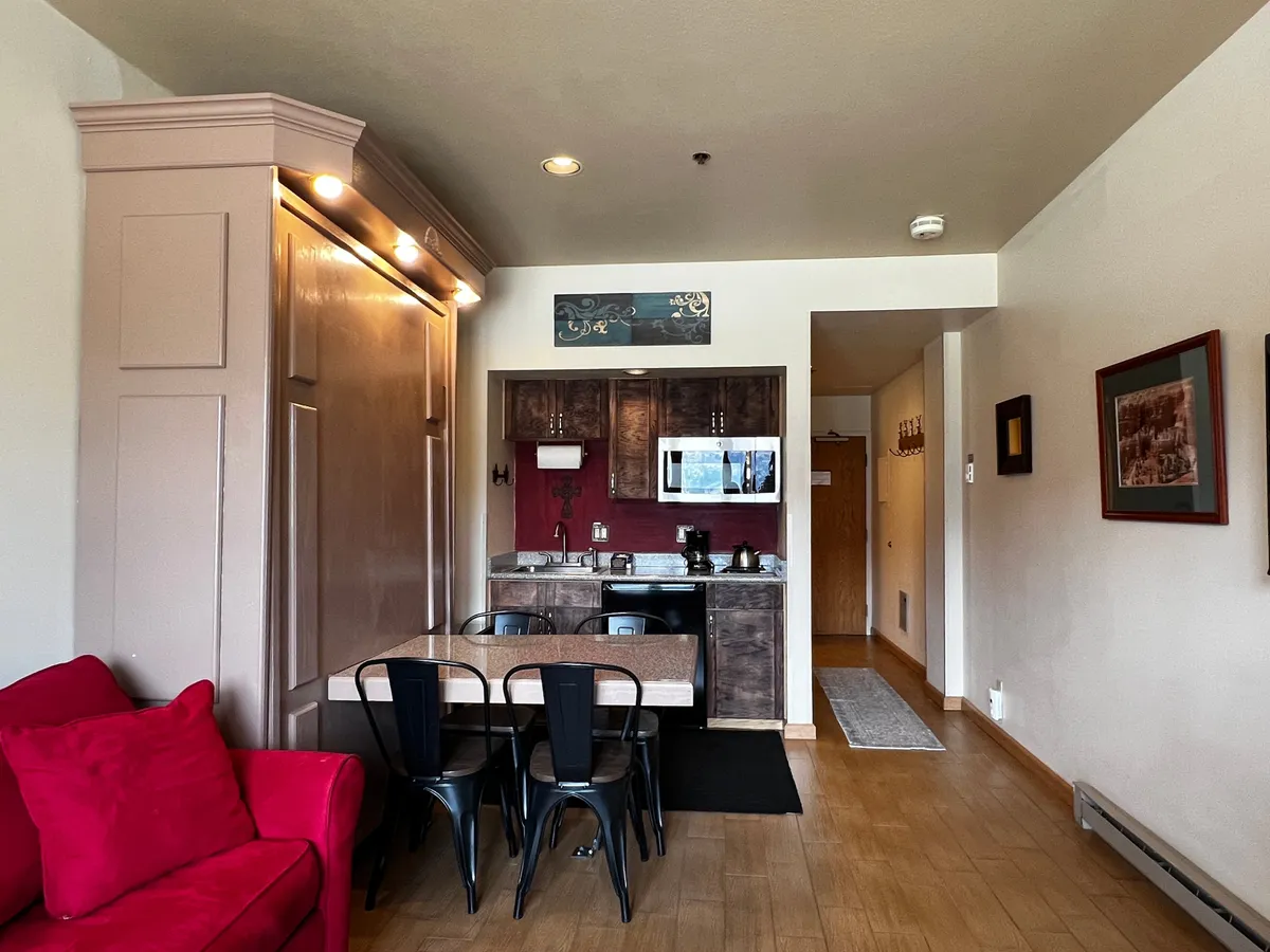 A welcoming living space featuring a red sofa, dining table, open kitchen area, and decorative wall art. The room is arranged for easy cooking, dining, and relaxing, with a social, casual atmosphere that promotes both work and leisure.